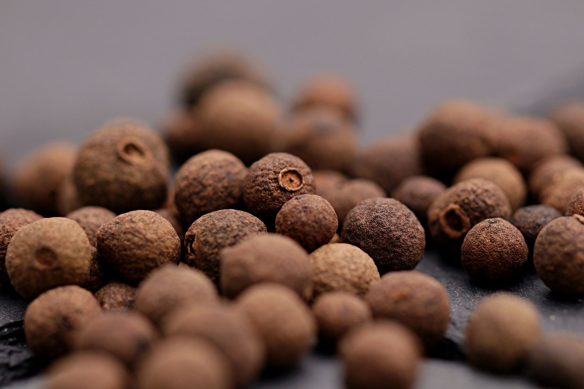 High-detail close-up of allspice peppercorns on a dark textured surface, showcasing natural textures.