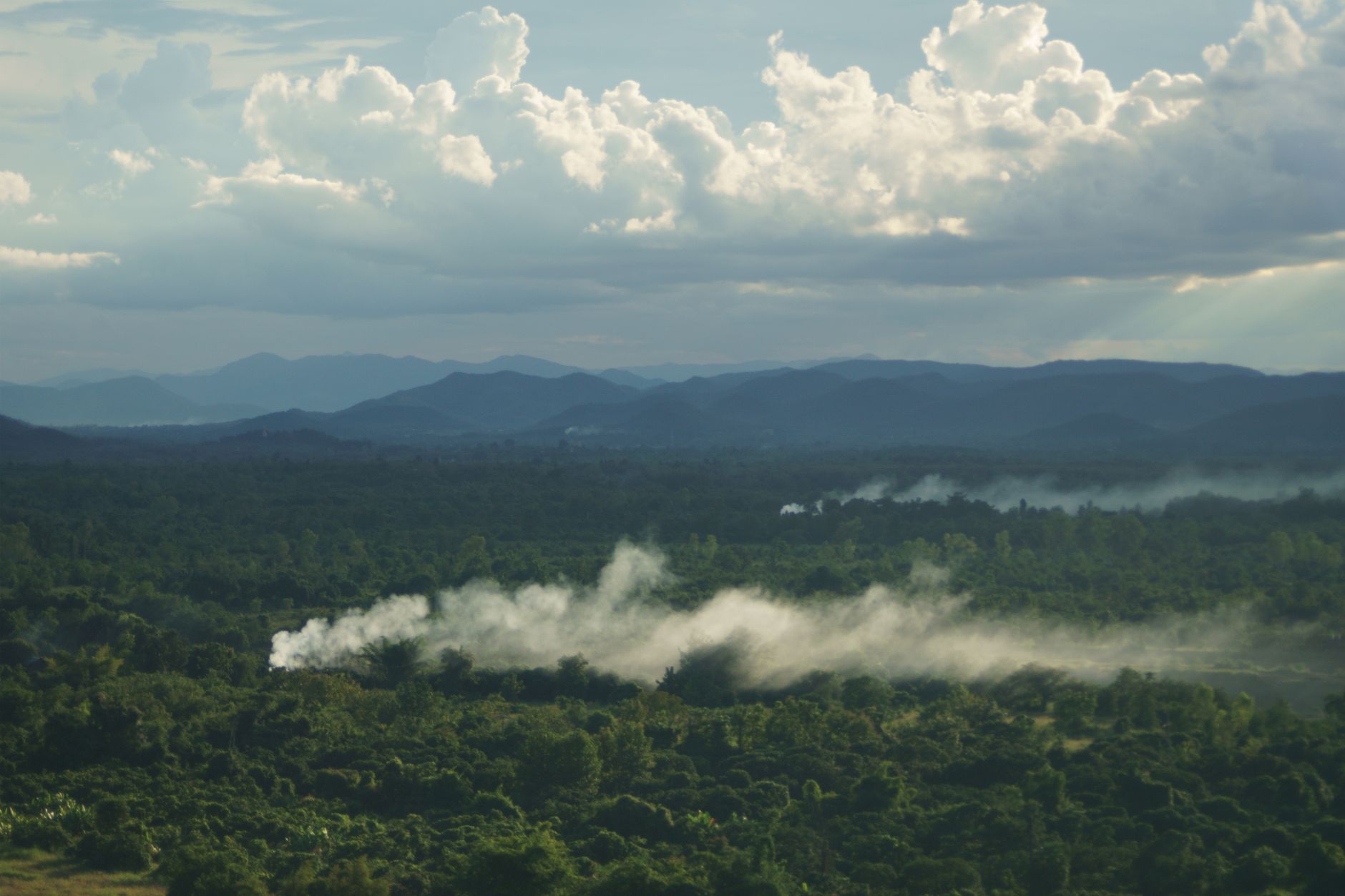 Dramatic aerial view of a forest landscape with mist, mountains, and clouds creating a serene atmosphere.